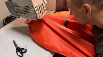 Toptrail maker feeding an orange pop-top canvas through a hot-air seam taping machine in the workshop in Latvia
