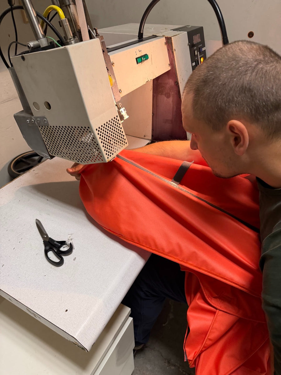 Toptrail maker feeding an orange pop-top canvas through a hot-air seam taping machine in the workshop in Latvia