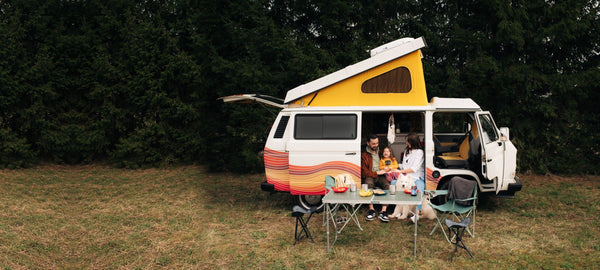 Family having lunch beside a white VW T3 Westfalia with a yellow Toptrail pop-top canvas
