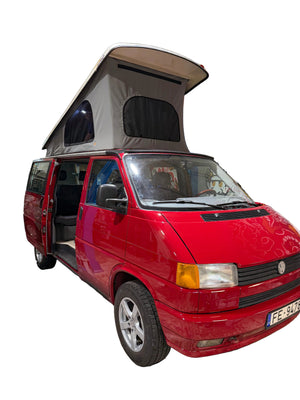 Van Volkswagen Transporter rouge, toit relevable ouvert, garé dans un garage avec la porte latérale ouverte.